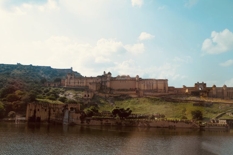 Wide view of Amer Fort in Jaipur overlooking Maota Lake with green hills in the background.