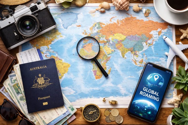 Flat lay of a world map with an Australian Passport, smartphone showing global roaming, camera, compass, and travel essentials